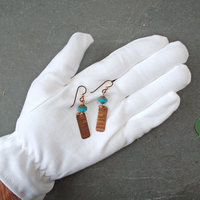 Earrings with corrugated copper rectangle dangles and turquoise Czech glass bead on top, in hand