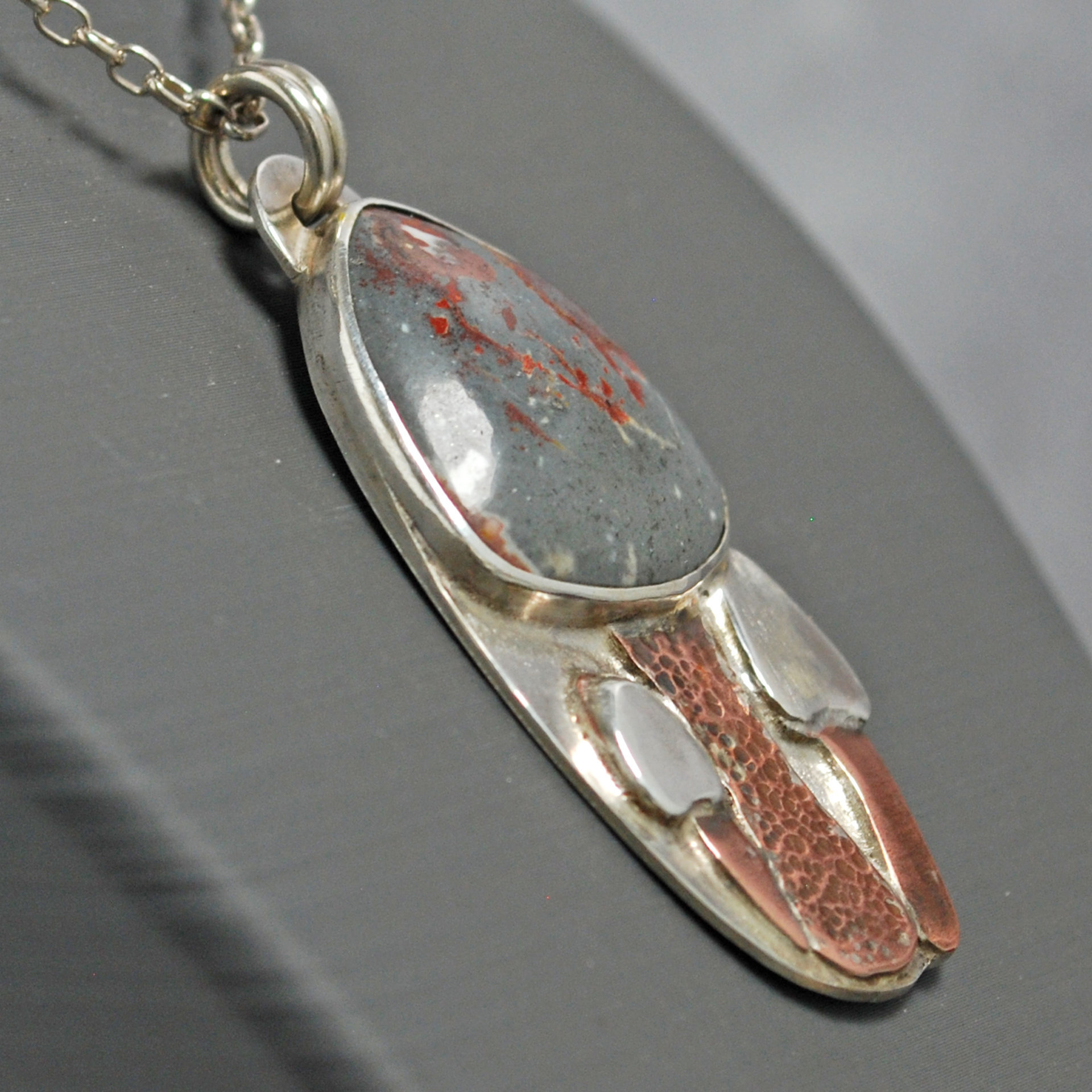Silver pendant with rhyolite "mushroom cap, copper mushroom stem, two additional silver and copper mushrooms, close up angle