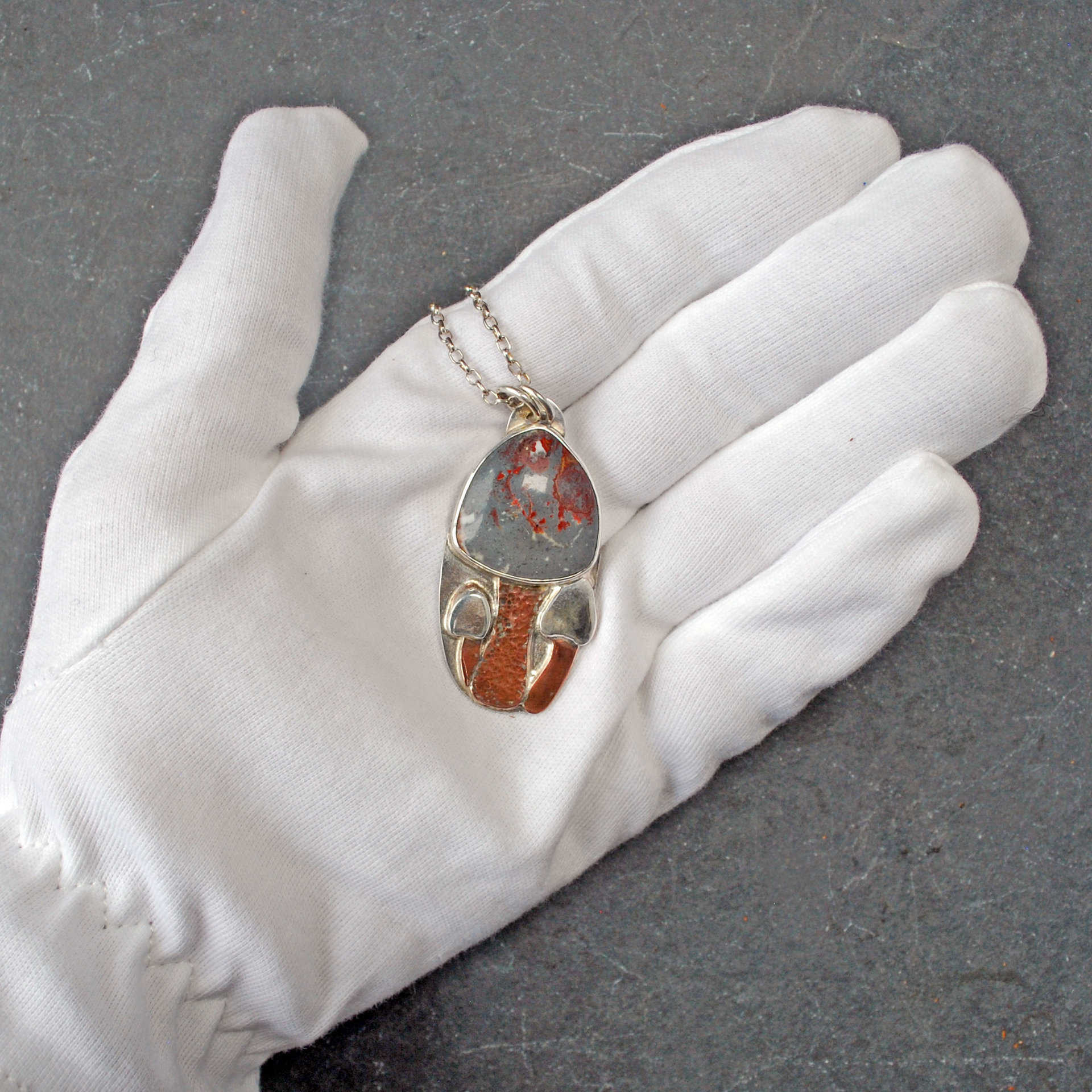 Silver pendant with rhyolite "mushroom cap, copper mushroom stem, two additional silver and copper mushrooms,  in hand