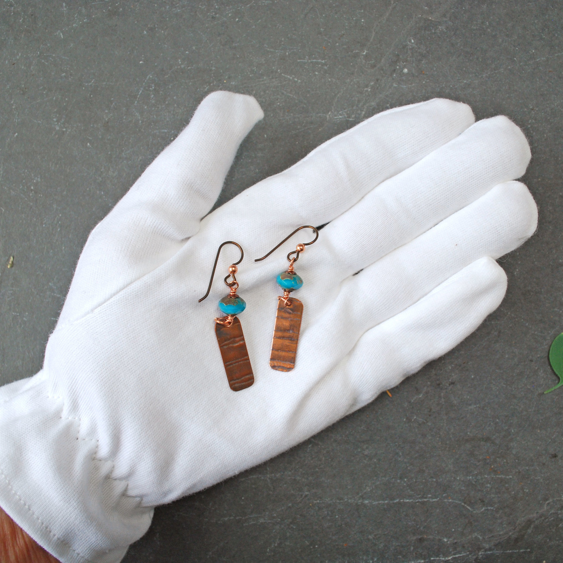 Earrings with corrugated copper rectangle dangles and turquoise Czech glass bead on top, in hand