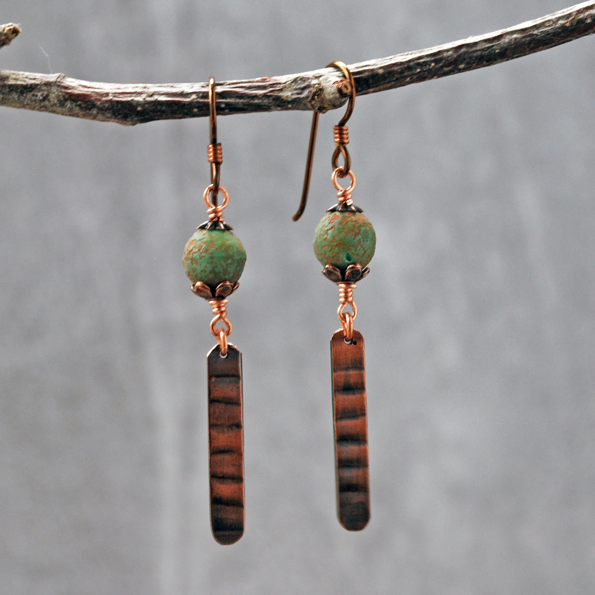 Earrings with green matte Czech glass on top, textured copper dangle below, hanging