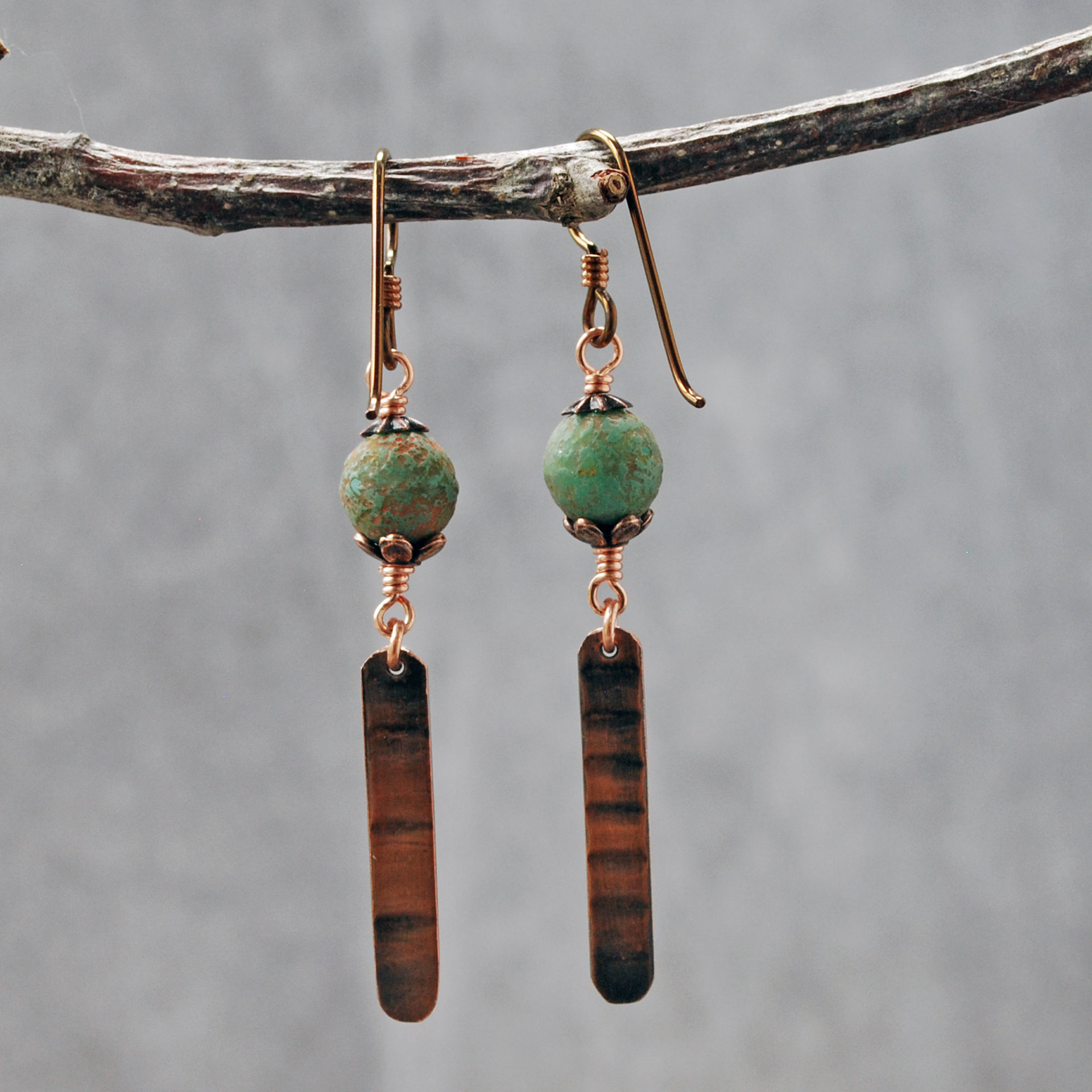 Earrings with green matte Czech glass on top, textured copper dangle below, hanging