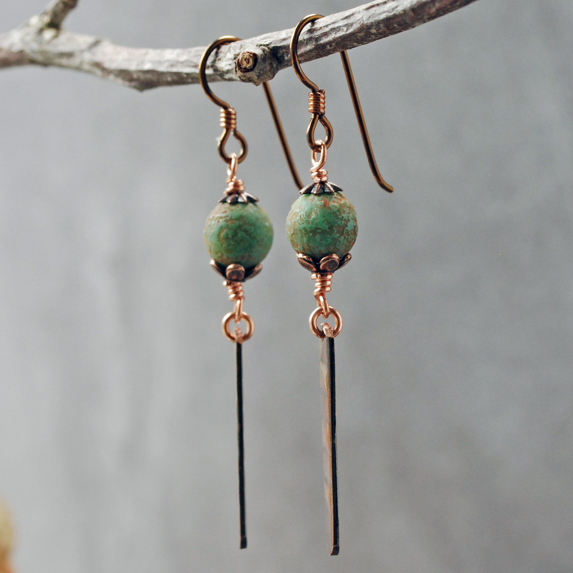 Earrings with green matte Czech glass on top, textured copper dangle below, hanging