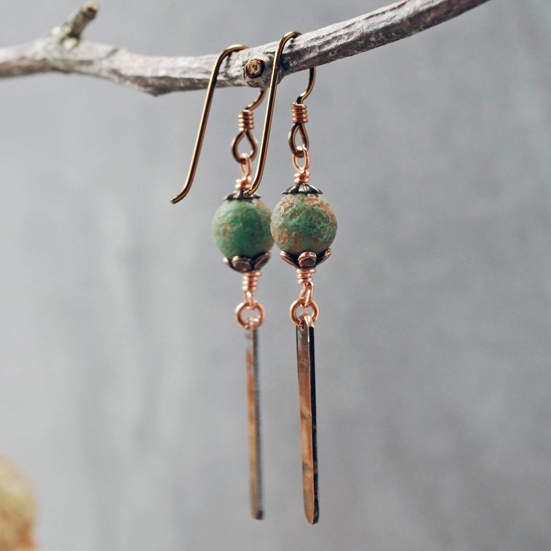 Earrings with green matte Czech glass on top, textured copper dangle below, hanging