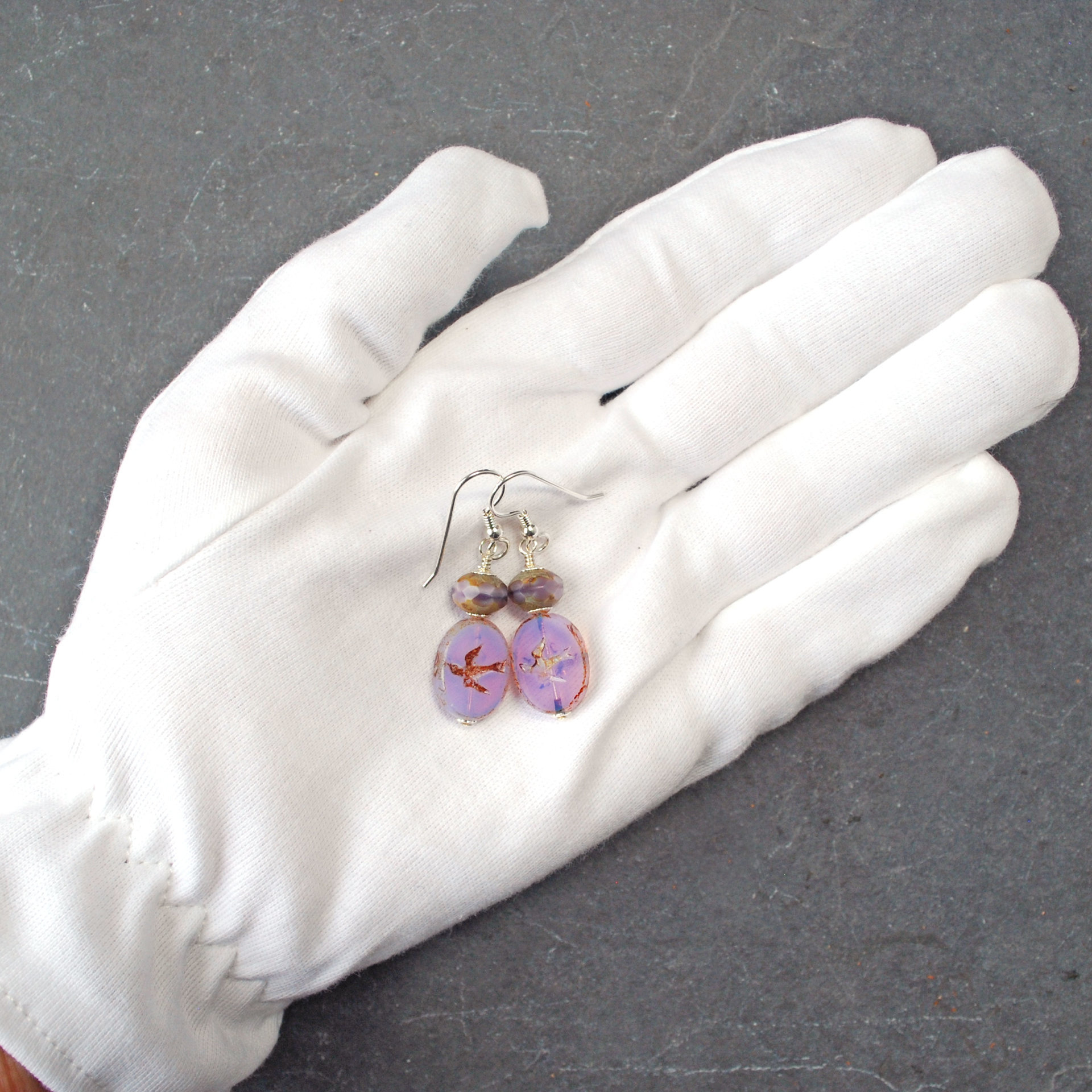 Pale purple Czech glass earrings, swallow embossed flat beads at bottom, topped by faceted rondelle beads, in hand